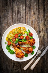 Fototapeta Barbecue chicken drumsticks with fried potato, lettuce and mini tomatoes on wooden table
 obraz