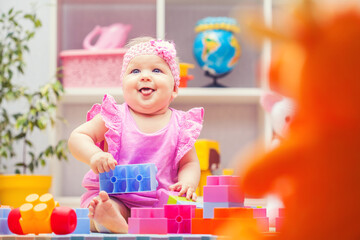 baby girl playing with colourful building blocks at home or kindergarten
