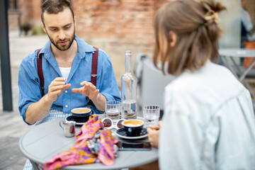 Stylish man talks with his female colleague while sitting and drinking coffee at cafe terrace outdoors. Business talk in relaxed atmosphere. Friends spending time together
