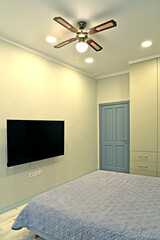 A fragment of the interior of a bedroom with a flat TV on the wall and a chandelier-fan on the ceiling