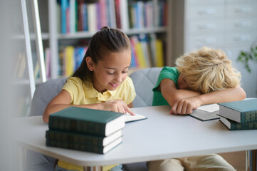 Fototapeta na wymiar Adolescent girl studying in the library beside her sleeping classmate