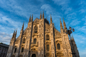 Sunset Scene of The ornate gothic facade, soaring spires and magnificent marble towers of the Duomo, Milan's monumental cathedral under big blue Lombardy skies - 522237276