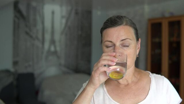 Senior woman taking vitamine supplement, medicine drug pill, drinking capsule with glass of water at home. Health care lifestyle, pharmacy and treatment therapy close up.