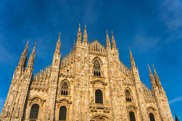Sunset Scene of The ornate gothic facade, soaring spires and magnificent marble towers of the Duomo, Milan's monumental cathedral under big blue Lombardy skies - 522237603