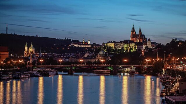 Prague, Czech Republic - Scenic View Of The Cathedral Of St. Vitus, Wenceslas And Vojtech From The River Illumined In Evening Lights With Ferries Sailing.  - Wide Shot