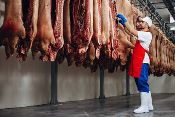 Man butcher standing by the hanging meat at the freezer