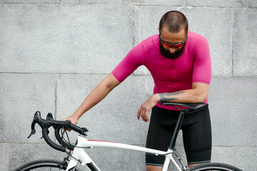 Naklejka na ściany i meble Cyclist in pink sportwear resting after an workout while standing against cement wall background with copy space area for text message or advertising