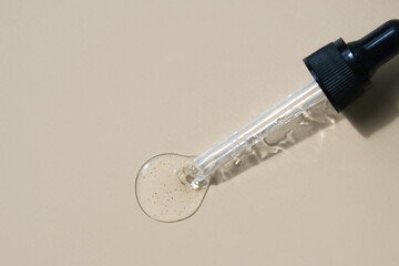 A drop of serum and a pipette on a beige background. Flat lay, place for text.