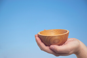 Plate in hand on a blue background similar to the sky. An empty wooden plate with a beautiful pattern on the hand in which you can put something.