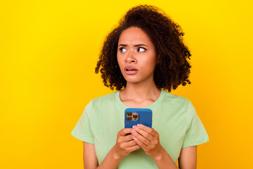 Fototapeta Photo of amazed confused girl dressed green t-shirt looking empty space holding modern device isolated yellow color background obraz