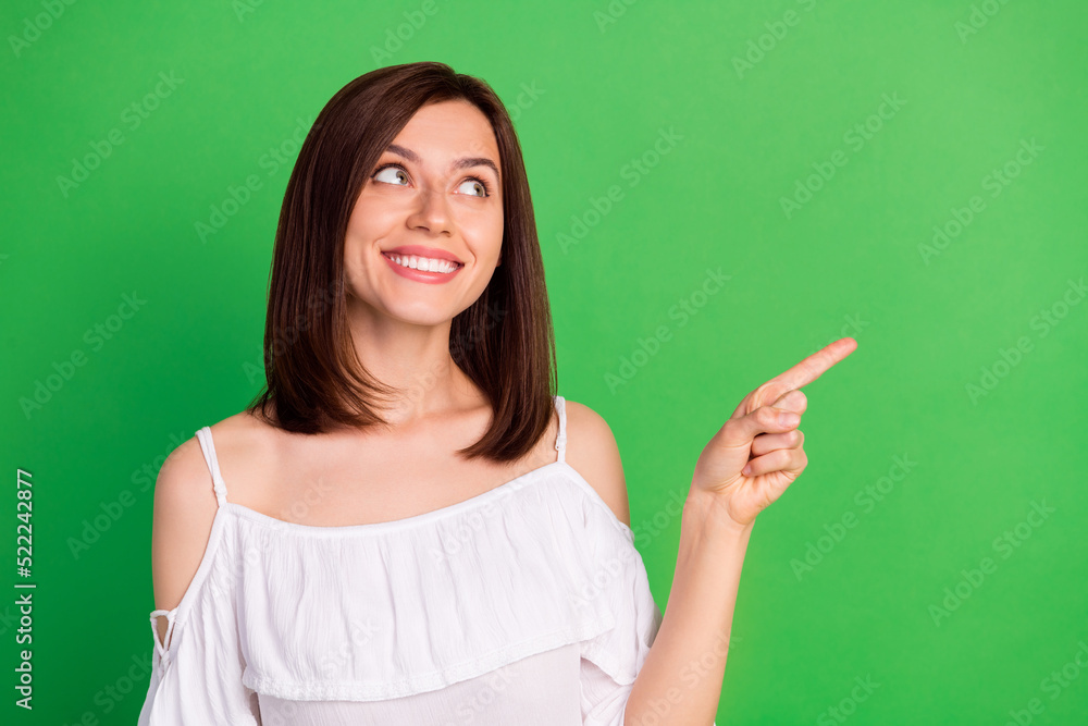 Wall mural photo of cheerful gorgeous lady toothy smile look indicate finger empty space isolated on green colo