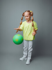 a little girl throws a ball up, isolated on a gray background. a little athlete.children's sports.