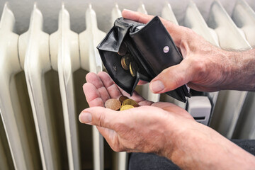 Hands of a man pouring out few coins from a wallet in front of an old heater, suffering from rising...