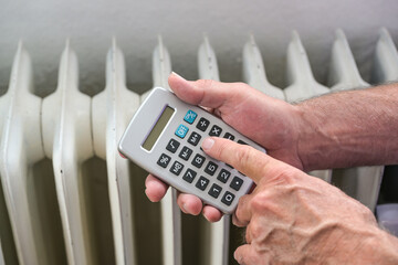 Hands of a man with a calculator figures out the energy costs of an inefficient heating system,...