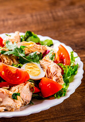 Fresh salad with fish, arugula, eggs,red pepper, lettuce, fresh sald leaves and tomato on a white plate on wooden table background - obrazy, fototapety, plakaty