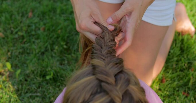 Kindergarten teacher braids a french braid for a girl outdoor