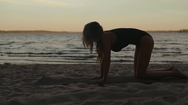 Beautiful and calm woman stretching on a sandy beach using a mat
