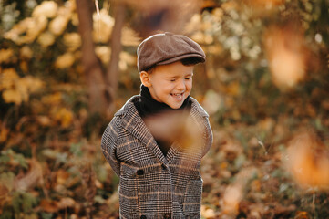 A happy candid baby boy is playing with yellow leaves in the golden autumn season in the park.