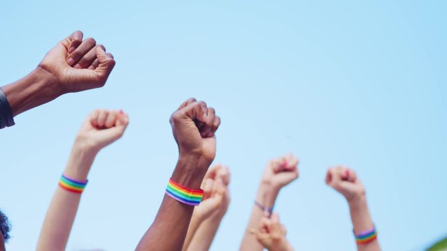 Cropped image of people raising arms with close fists wearing a lgbt bracelet