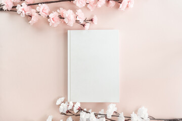 White book mockup on a pastel pink background with white and pink cherry blossom. Education,...