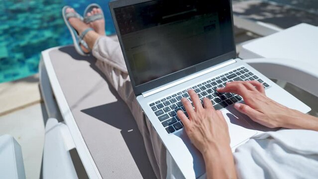 Faceless Female Using Laptop Computer Online Internet While Lying On Sun Loungers By Swimming Pool Of Resort Hotel.