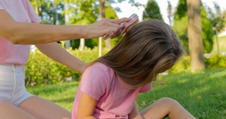 Mother combing her daughter's hair outdoor