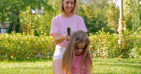 Mother combing her daughter's hair outdoor