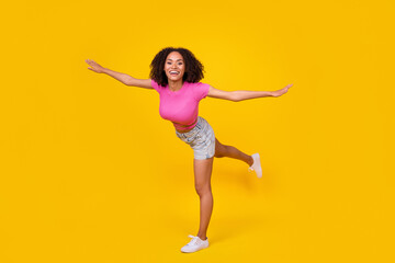 Fototapeta na wymiar Full size portrait of cheerful adorable girl arms wings stand one leg isolated on yellow color background