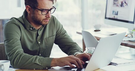Serious man thinking and typing on a laptop while working in a creative office. Male web designer adjusting his glasses while communicating about problem and sending email about ideas for a design - Powered by Adobe