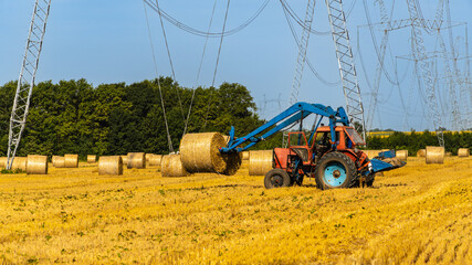 Straw bales on universal forks mounted on a Belarus or Petushok tractor. Collection of hay bales in one place for transportation. Rolls with straw under VL-750. Smolenskaya, Russia - July 16, 2022