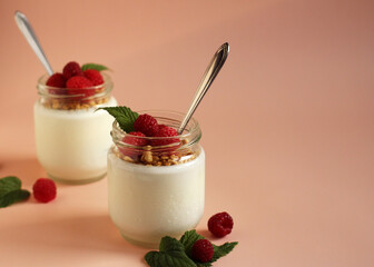 natural white yogurt in a glass jar with raspberries, muesli and metal spoon
