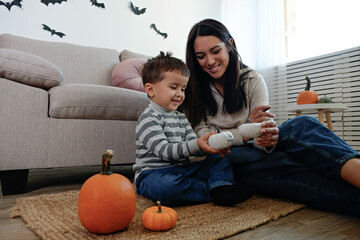 Young beautiful woman with her three year old son preparing decorations for halloween at home. Mom...