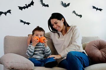 Young beautiful woman with her three year old son preparing decorations for halloween at home. Mom...