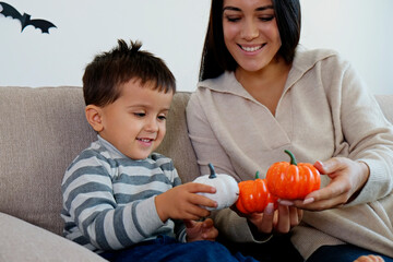 Young beautiful woman with her three year old son preparing decorations for halloween at home. Mom...