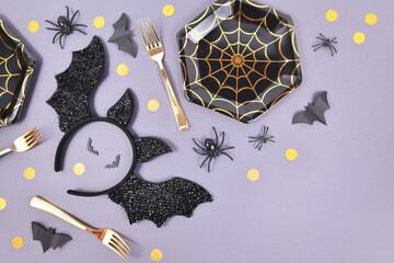 Halloween party flat lay with spider web plates, costume bat headband, spiders and confetti on...