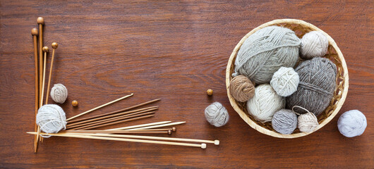 Composition of balls of natural wool yarn in a wicker basket and a set of knitting needles and crochet hooks on a wooden table. Craft and DIY concept. Flat lay, copy space, top view, blank, mock up