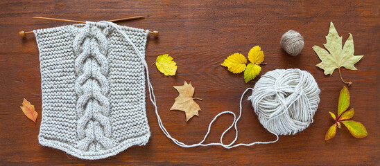 Autumn needlework. Top view of knitting a warm scarf with a braid made of natural wool yarn, bright fallen autumn leaves on a wooden background. Craft and DIY concept. Flat lay, closeup
