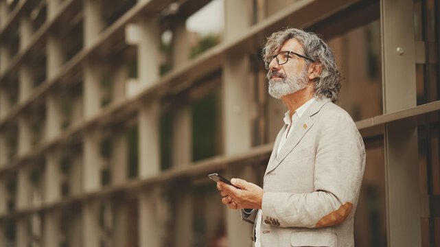 Fototapeta Profile mature businessman with beard in eyeglasses wearing gray jacket looking up at street signs and map trying to find her way using cellphone