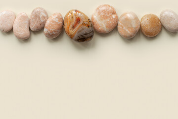 Top view close up colored pebbles sea stones on sand color background. Row from natural round smooth stone neutral tones and sardonyx. Minimal style flat lay, summer concept, empty space