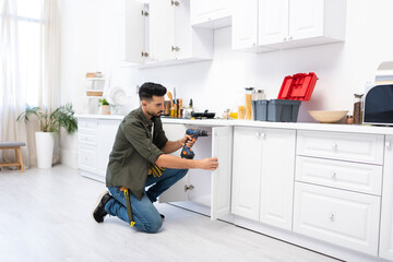 Young arabian man with screwdriver fixing door of kitchen cabinet - Powered by Adobe
