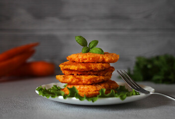 natural dietary carrot pancakes on a plate with lettuce leaves and a fork on a gray background - obrazy, fototapety, plakaty