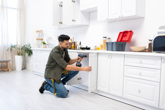 Young arabian man with screwdriver fixing door of kitchen cabinet