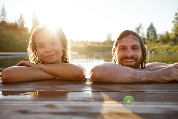 Summer portrait of young couple swimming in lake lit by Sunlight and smiling