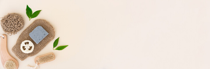 Bath accessories for home skin care and scrubbing procedure - bath gloves, wooden brushes, hemp bath cloth, loofah sponge and organic soap scrub over light background with copy space. Flat lay banner