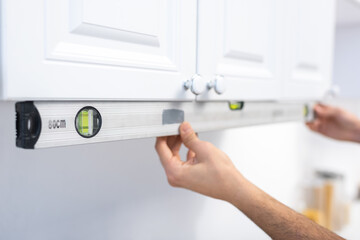 Cropped view of man holding spirit level near kitchen cabinet