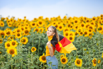 Blond girl holding waving flag of Germany in the sunflower field. Day of German Unity. Travel and...