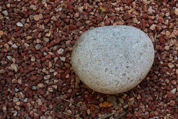 Round stone lies on decorative pebbles of red color.