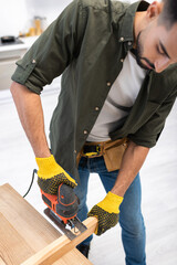 High angle view of young muslim carpenter holding jigsaw machine near wooden board at home