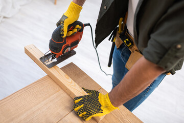 High angle view of carpenter in gloves sawing wooden board on table at home