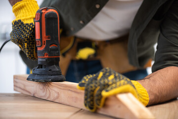 Cropped view of carpenter sanding wooden plank with tool at home
